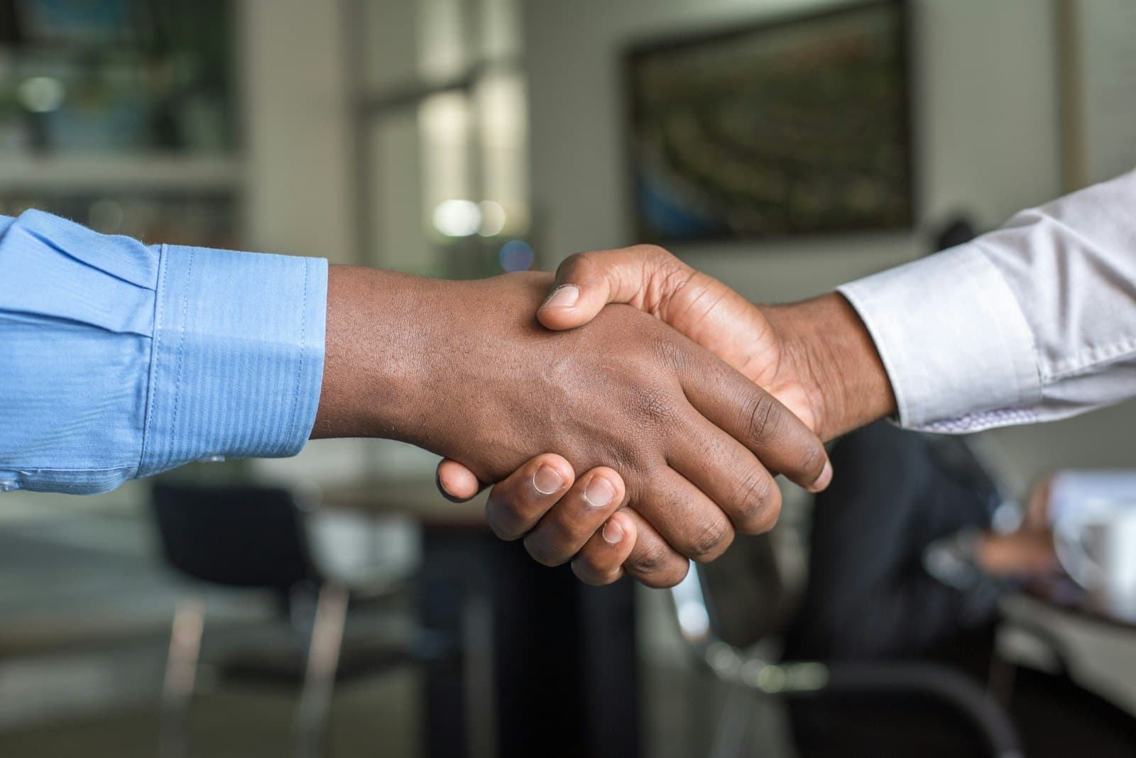 Two people shaking hands across a desk after closing a deal